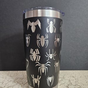 Puede incluir: Un vaso de acero inoxidable negro con un dise&ntilde;o de telara&ntilde;a. El vaso tiene una tapa plateada y una base plateada.