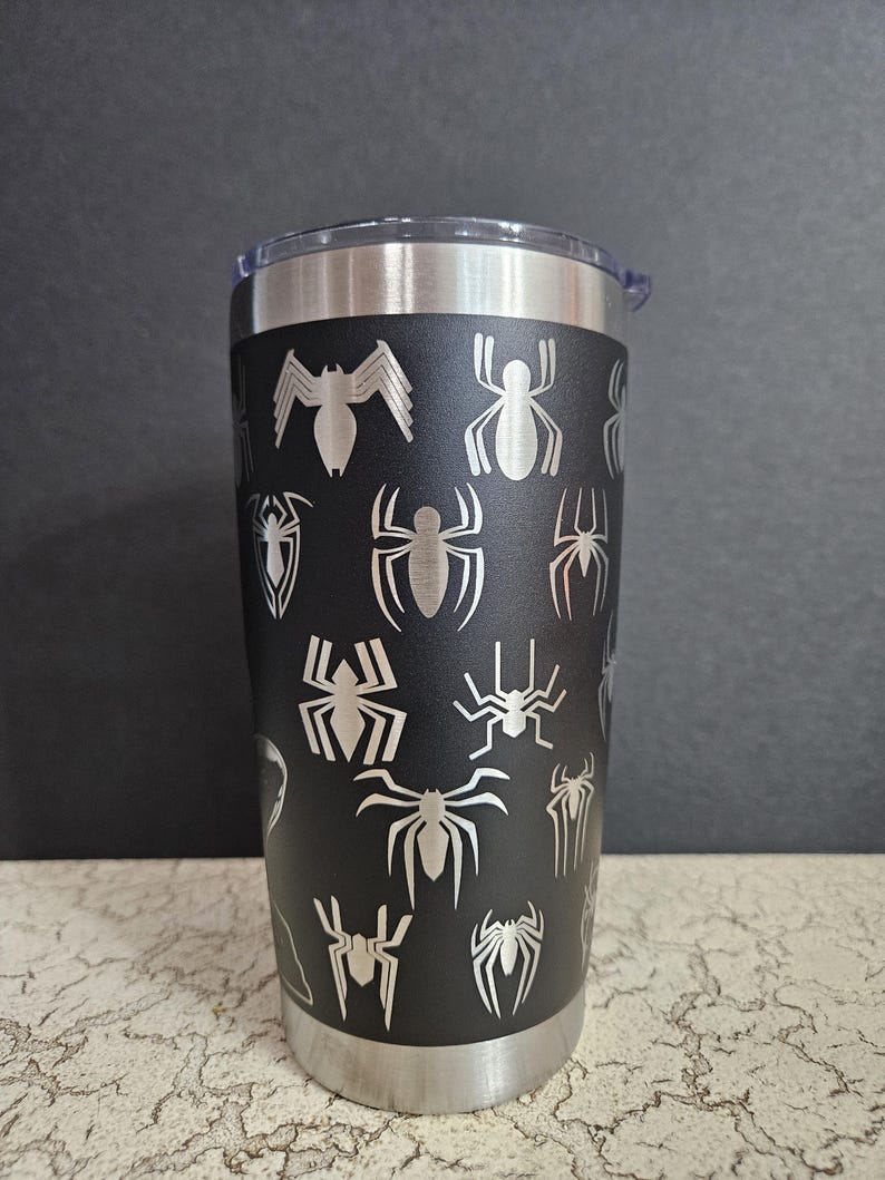 Puede incluir: Un vaso de acero inoxidable negro con un dise&ntilde;o de telara&ntilde;a. El vaso tiene una tapa plateada y una base plateada.