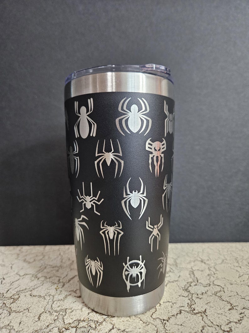 Puede incluir: Un vaso de acero inoxidable negro con un dise&ntilde;o de telara&ntilde;a. El vaso tiene una tapa plateada y una base plateada.
