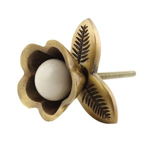 May include: A decorative brass flower-shaped cabinet knob with a white, spherical center. The knob features detailed leaf-like engravings on the petals and a threaded screw for installation. The overall design is vintage-inspired.