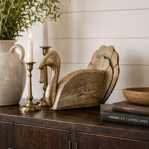 May include: A decorative turkey figurine crafted from wood with a distressed gold-toned finish. The bird features a curved neck, a prominent wattle, and a fanned tail design. The surface shows natural wood grain textures beneath the metallic paint.