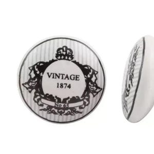 May include: A white ceramic button with a black and white design. The design features a crown, a banner with the text "Vintage 1874", and the text "No 65".