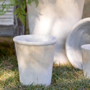 May include: A set of three white ceramic planters with a distressed finish. The planters are different sizes and shapes, and they are all sitting on a bed of green grass.