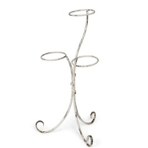 May include: A distressed white metal plant stand with three circular holders. The stand has a curved design with decorative scrollwork at the base. The stand is designed to hold multiple plants.