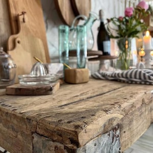 May include: A close-up of a rustic wooden table with metal accents. The table is made of reclaimed wood and has a natural, weathered finish. The metal accents are in the shape of squares and are attached to the edges of the table.