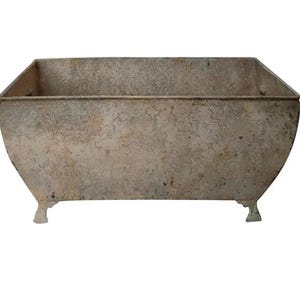 May include: A weathered, rectangular planter with a distressed, light brown finish. The planter has four short legs and a slightly rounded bottom.