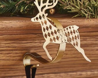 May include: A gold-colored metal stocking holder shaped like a reindeer. The reindeer has a diamond-patterned body and is attached to a curved hook. The hook is designed to hang on a mantel or shelf. Decorative holiday item.