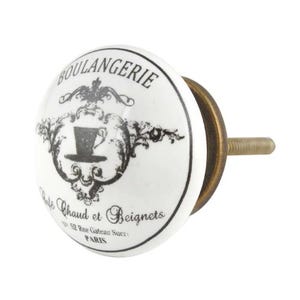 May include: White ceramic cabinet knob with a black and white design featuring the text "Boulangerie Cafe Chaud et Beignets 52 Rue Gateau Sucrer PARIS".