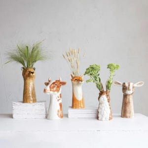 May include: Five ceramic animal head vases with different floral arrangements. The vases are in the shapes of a fox, a cow, a rabbit, a goat, and a lion.