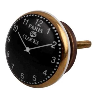 May include: Black and gold ceramic cabinet knob with a clock face design. The clock face has white numbers and hands, and the text "Paris Clocks" in the center.