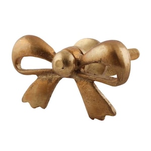 May include: Gold-toned metal bow-shaped cabinet knob with a textured finish.
