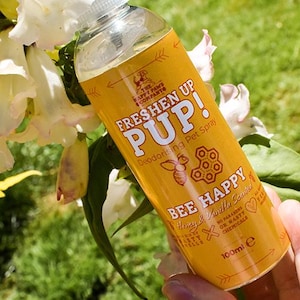 Könnte beinhalten: Gelbe Sprühflasche mit einem Etikett, auf dem "Freshen Up Pup!" Deodorierendes Haustier-Spray Bee Happy Honig & Vanille Duft steht. Das Etikett trägt außerdem die Aufschrift "Ohne Parabene oder schädliche Chemikalien" und "100 ml e".