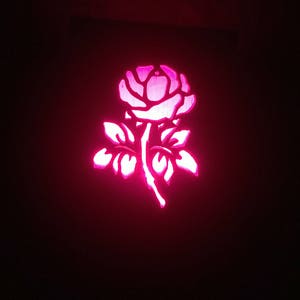 May include: A pink rose cut out of wood and illuminated from behind, creating a glowing effect.