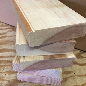 May include: A stack of four unfinished wooden boards with a natural wood grain. The boards are stacked on top of each other, with the top board being the largest. The boards are all the same width, but the top board is slightly longer than the others.