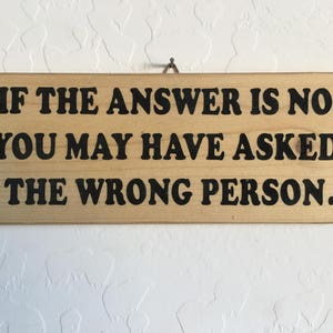 May include: Wooden sign with the text "If the answer is no, you may have asked the wrong person."