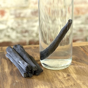 May include: A glass jar filled with water and a long, thin black charcoal stick. A bundle of four smaller charcoal sticks are on a wooden surface.