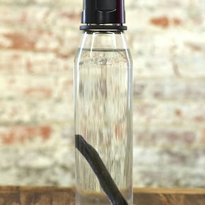 May include: A clear glass bottle with a black lid and a black charcoal stick inside. The bottle is sitting on a wooden surface.