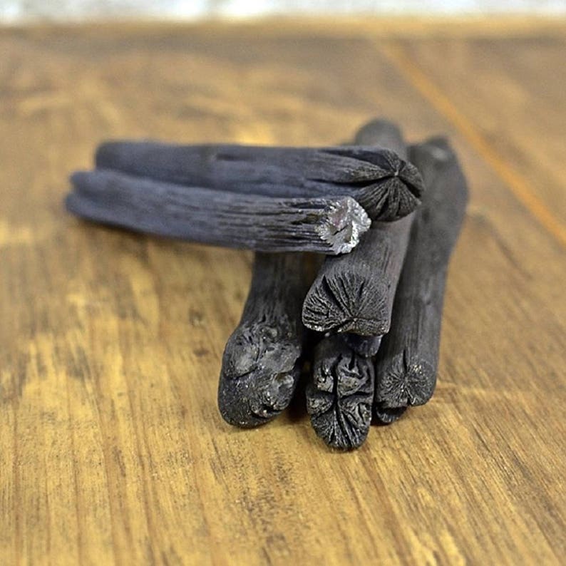 May include: A close-up of a pile of black charcoal sticks on a wooden surface. The sticks are arranged in a random pattern, and some of them are broken.