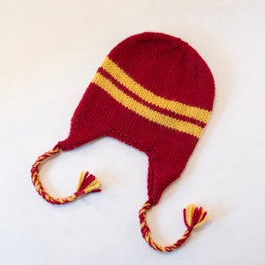 May include: Red knitted hat with yellow stripes and long tassels. The hat has a pointed top and ear flaps.