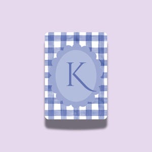 Könnte beinhalten: Eine rechteckige Karte mit blau-weißem Vichy-Karo-Hintergrund. Ein hellblaues, geschwungenes Oval in der Mitte enthält den Buchstaben "K" in dunklerem Blau. Die Karte hat abgerundete Ecken.