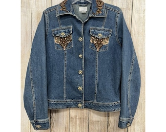 May include: A blue denim jacket with brown and gold embroidered details on the collar and pockets. The jacket has a button closure and long sleeves.