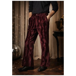 May include: Burgundy velvet pants with a flared leg. The pants have a high waist and a button closure. The fabric has a textured appearance. The pants are paired with black shoes and a black long-sleeve shirt.