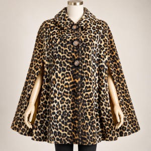 May include: A leopard print cape featuring a rounded collar and three large, dark brown circular buttons down the front. The garment has a flared silhouette with open arm slits on the sides, showcasing a solid tan lining on the interior.