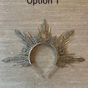 May include: A silver-toned crown with intricate filigree and geometric designs. The crown features a halo-like structure with radiating elements and is labeled "Option 1".