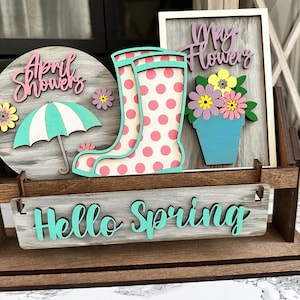 May include: Wooden spring-themed decor with a sign that says "Hello Spring", a round sign that says "April Showers", a sign that says "May Flowers" with a flower pot and flowers, and a pair of pink rain boots with white polka dots.