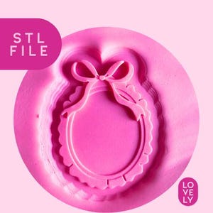 May include: A pink, 3D-printed mould featuring a bow and a scalloped frame design. The text "STL FILE" is in the upper left corner. The word "LOVELY" is in the lower right corner.