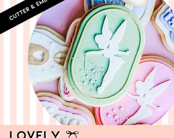 Op de afbeelding: Een set koekjesuitstekers en -embossers met een fee-ontwerp. De uitstekers zijn gemaakt van lichtgroen en roze plastic. De uitstekers hebben de vorm van een fee met vleugels en een toverstaf. De uitstekers bevinden zich op een roze en wit gestreepte achtergrond.