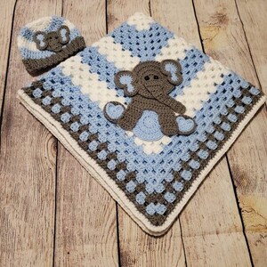 May include: A crocheted baby blanket in shades of blue, white, and gray with a gray elephant applique. A matching crocheted hat with an elephant applique is included.