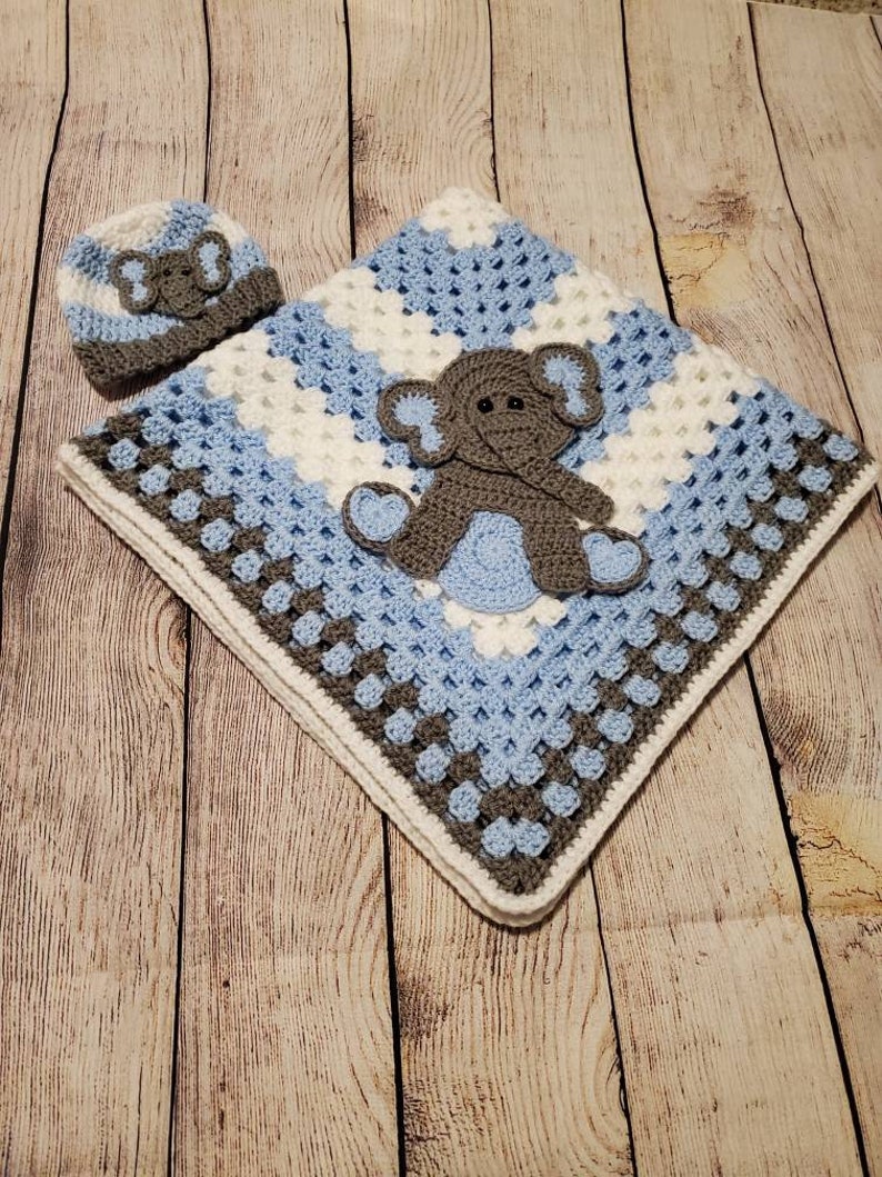 May include: A crocheted baby blanket in shades of blue, white, and gray with a gray elephant applique. A matching crocheted hat with an elephant applique is included.