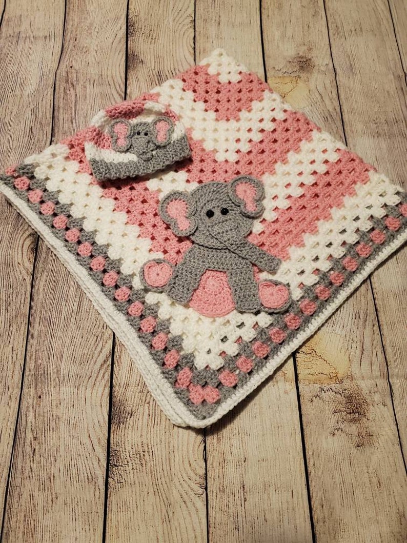 May include: A pink and white crocheted baby blanket with a gray elephant applique and a matching crocheted hat.