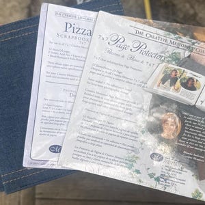 Könnte beinhalten: Ein Stapel Scrapbooking-Zubehör, darunter ein mit Denim bezogenes Album und zwei Packungen Creative Memories 17,78 cm x 17,78 cm Seitenschutzhüllen und Scrapbook-Seiten. Die Verpackung zeigt Text und Bilder.