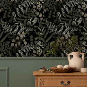 May include: Dark wallpaper with a repeating pattern of green and tan leaves and foliage. A wooden dresser with a vase, bowl, and small dish is in front of a green wall. The vase is white and has two handles.