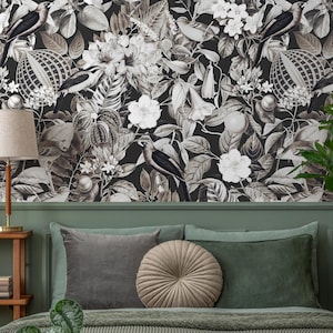 Könnte beinhalten: Schwarz-weiße florale Tapete mit Vögeln, Blumen und Blättern. Die Tapete befindet sich über einem Bett mit grauen und grünen Kissen, einem runden beigen Kissen und einer grünen Tagesdecke. Eine Lampe und eine Topfpflanze sind ebenfalls zu sehen.