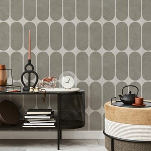 May include: A modern interior scene featuring a gray and white patterned wallpaper. A black console table displays decorative items like a candle holder, clock, and books. A small table holds a teapot and cup, with a layered ottoman in the foreground.