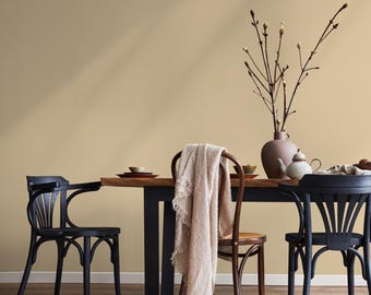 May include: A dining room scene featuring a wooden table with black legs, set with plates, a teapot, and a vase with branches. Three chairs, two black and one brown, are positioned around the table. A beige throw blanket hangs on one of the chairs.