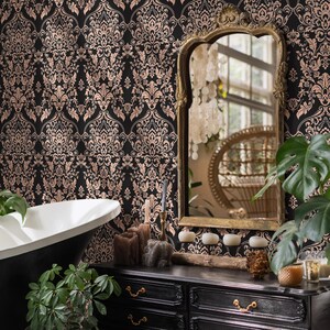 May include: A black and gold damask wallpaper with a white bathtub and a black vanity with gold hardware. The vanity has three drawers and is decorated with candles, a wooden log, and a pine cone.
