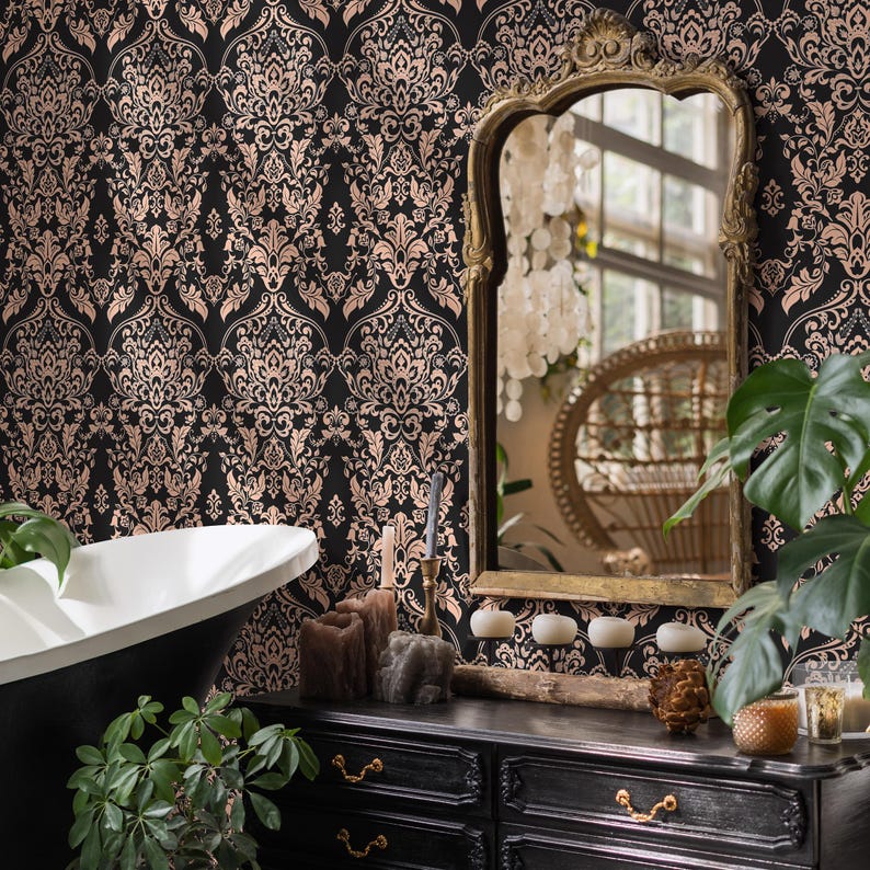 May include: A black and gold damask wallpaper with a white bathtub and a black vanity with gold hardware. The vanity has three drawers and is decorated with candles, a wooden log, and a pine cone.