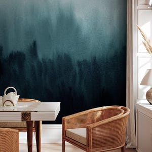 May include: A teal and navy blue watercolor mural creates a serene backdrop. A white table with a teapot and cups sits in front of the mural. A rattan chair with a beige cushion adds a natural element to the room.