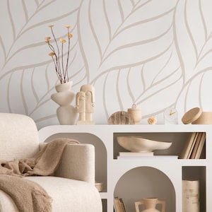 May include: A neutral-toned interior scene featuring a white cabinet with arched cutouts, a cream-colored armchair, and a beige throw blanket. Decorative items include a vase with dried stems, sculptures, and a small clock. The backdrop is a white wall with a beige leaf pattern.