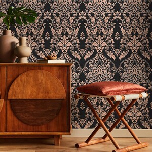 May include: A dark brown wooden cabinet with a half-circle design on the front door. The cabinet is in front of a wall with a black and pink damask wallpaper pattern. A wooden stool with a red cushion sits in front of the cabinet.