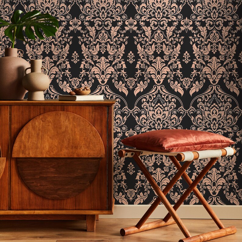 May include: A dark brown wooden cabinet with a half-circle design on the front door. The cabinet is in front of a wall with a black and pink damask wallpaper pattern. A wooden stool with a red cushion sits in front of the cabinet.