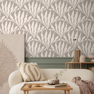 Puede incluir: Interior de salón con sofá beige, cojín estampado y mesa de centro de madera. La pared está decorada con papel pintado con motivos blancos en forma de hojas sobre fondo gris. Decoración adicional: una obra de arte en lienzo y un jarrón.
