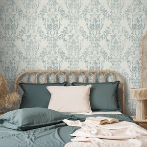 May include: A bed with a teal blue duvet cover and matching pillowcases. The headboard is made of woven wicker and the bed is styled with a white throw blanket and a book. The wall behind the bed is covered in a light blue and white damask wallpaper.
