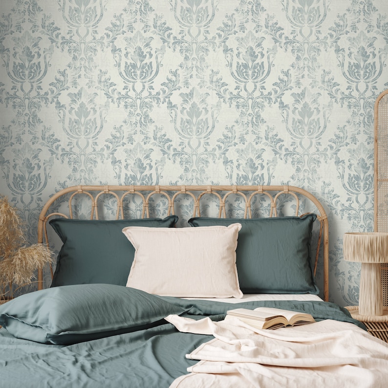 May include: A bed with a teal blue duvet cover and matching pillowcases. The headboard is made of woven wicker and the bed is styled with a white throw blanket and a book. The wall behind the bed is covered in a light blue and white damask wallpaper.