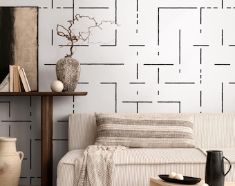 May include: A modern living room scene featuring a white sofa with a striped pillow and a beige throw. The wall has a black geometric pattern. A wooden side table holds a vase, books, and a decorative sphere. A black pitcher and tray are on a wooden coffee table.