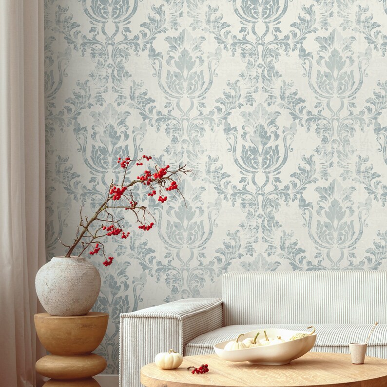 May include: A living room interior with a light blue damask patterned wallpaper, a white couch, a wooden coffee table, a ceramic vase with red berries, and a wooden stool.